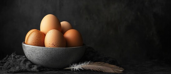 Leinwandbilder - Brown eggs in a gray ceramic bowl A bird feather and one egg on the table Black background Copy space