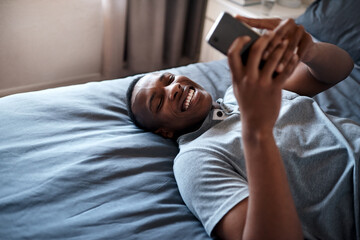 Happy, laugh and black man on bed with phone for social media, online chatting and internet in bedroom. Relax, rest and person on smartphone for website, networking and message on weekend in home