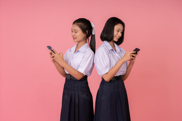 The studio photo showcases two Asian school girls, their high school uniforms perfectly framing their bright smiles against a charming pink background that embodies the spirit of their teenage years.