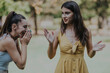 © qunica.com - Two young women share a fun moment at the park, expressing happiness and friendship. They appear relaxed and joyful, embodying a carefree and friendly atmosphere in an outdoor setting.