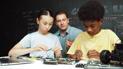 Smart mentor teach main board construction while diverse teenager learning system. Teacher explain about motherboard structure while academic student learning to use electronic equipment. Edification.