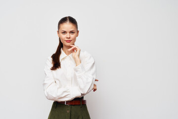 Canvas Print - Young woman in a white shirt with a thoughtful expression on a plain white background, dressed in stylish green pants, showcasing confidence and poise