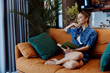 © SHOTPRIME STUDIO - Woman reading book while sitting on couch with plant in front of her in cozy living room setting