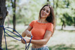 © qunica.com - A young woman smiling as she sets up a hammock in a green park on a sunny day. The atmosphere is cheerful and relaxed.