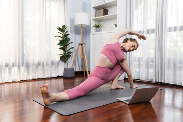 Flexible and dexterity woman in sportswear doing yoga position in meditation posture on exercising mat at home. Healthy gaiety home yoga online training session with peaceful mind and serenity.