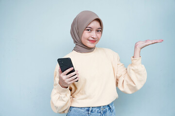 Smiling Asian muslim woman in cream sweater and hijab using a mobile phone, showing copy space on hands isolated over white background. People religious lifestyle concept.