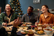 © Seventyfour - Diverse group of four cheerful friends laughing while chatting at festive dining table celebrating Christmas together at home dinner