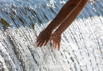 Wall Mural - A person is reaching into a waterfall to touch the water