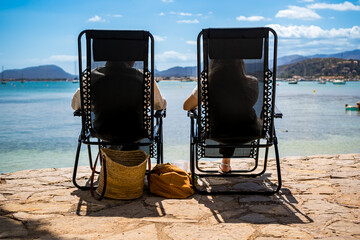 Passeig de Colom promenade in Puerto de Pollensa, Mallorca, with two unrecognizable people in lounge chairs enjoying the day, for travel content focused on relaxation, privacy and idyllic retreats.