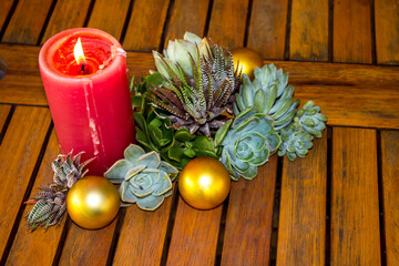 A Christmas still-life consisting of a lit candle, various succulents and golden balls, on a rustic wooden table.