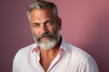 A man with a beard and gray hair is wearing a white shirt and pink collar