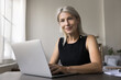 © fizkes - Portrait smiling confident 60 years old lady freelancer teacher remote worker sit at home office work desk by modern laptop look at camera. Smart successful aged woman enjoy easy distant job using pc