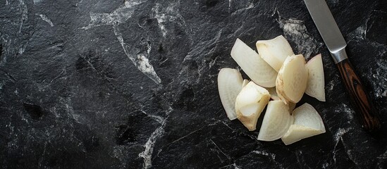 Poster - Peeled daikon radishes and a knife resting on a black stone countertop viewed from above for copy space