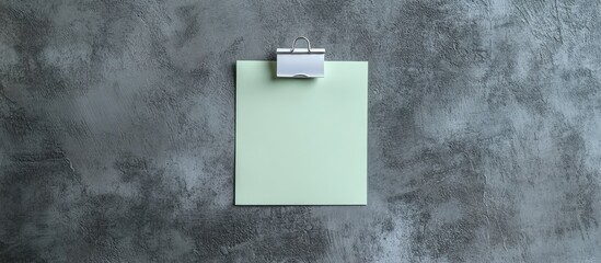 Poster - Blank light green note with a white paper clamp on a grey background viewed from above Space for text. with copy space image. Place for adding text or design