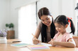 © NAMPIX - Asian mother helping her daughter with homework, sitting in living room interior, copy space.