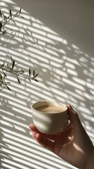 Poster - A hand holding a white cup of coffee near a window with sunlight creating striped shadows