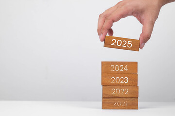 A hand placing a wooden block labeled '2025' on top of stacked blocks representing previous years. Symbolizes progress and planning.