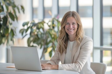 Poster - A businesswoman in a bright office environment smiles confidently while working on her laptop, exuding professionalism, positivity, and modern work culture.