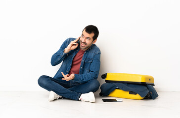 Wall Mural - Caucasian handsome man with a suitcase full of clothes sitting on the floor at indoors keeping a conversation with the mobile phone with someone