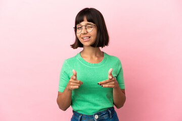 Young mixed race woman isolated on pink background pointing to the front and smiling