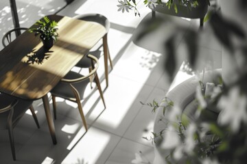 Table with four chairs and a potted plant in front of it. The room is bright and sunny, with a lot of natural light coming in from the windows. The potted plant adds a touch of greenery to the space