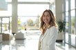 © Odin AI - A woman in a white blazer stands confidently in a sunlit office lobby, radiating positivity and professionalism. The modern setting enhances her approachable demeanor.