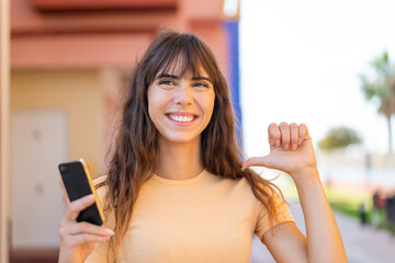 Young woman using mobile phone at outdoors proud and self-satisfied