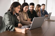 © fizkes - Three multiethnic young adult students studying at laptop in educational center, sitting at computer together, pointing at screen, laughing, smiling, writing notes. Colleagues analyzing online startup