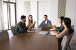 © fizkes - Positive young diverse business colleagues meeting at large table for teamwork, cooperation, brainstorming on creative project, talking in collaboration room, discussing ideas, marketing strategy