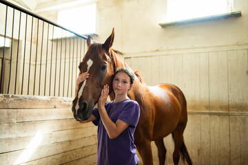 Teenage Girl Cares for a Brown Horse in Stall in Barn