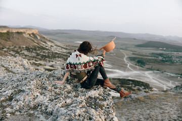 Wall Mural - Majestic woman in hat sitting atop mountain, gazing over expansive valley below