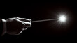 © Oksana - A hand holds a wand against a dark background, creating a bright light. Concept of magic and mystery. For fantasy and magical themed content.