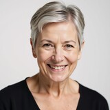 An older woman grey-haired with a smile poses wearing only a black bra