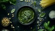 © Arifin Studio - A bowl of fresh pesto surrounded by ingredients like basil, pine nuts, Parmesan cheese and spaghetti on a dark background.