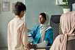 © pressmaster - Muslim doctor in hijab engaging with a patient during consultation in clinic, wearing stethoscope. Scene includes diverse setting and healthcare setting in background