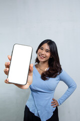 isolated portrait of a teenage woman standing with showing mobile phone screen for an advertisement, she is wearing a tight blue casual top and loose hair, advertising Asian women