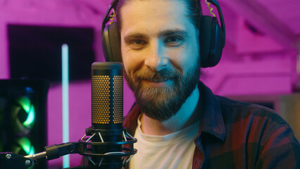 Happy Caucasian man carefree gamer male guy influencer in headphones cyber sport radio blogger talking in microphone stream online on Internet broadcast content home neon popular streamer speak smile