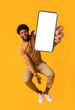 © Prostock-studio - Excited black guy holding smartphone, showing blank screen, jumping up over orange studio background. Handsome african american young man recommending new mobile application, collage