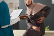 © pressmaster - Muslim female patient wearing hijab sitting in clinic during medical consultation, engaging with healthcare professional holding a clipboard