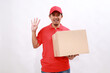 © ArvStd - Happy asian delivery courier in red t-shirt and cap carrying a box package while showing four fingers. isolated over white background