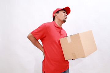 Asian delivery courier in red t-shirt and cap having back ache while carrying a box package. isolated over white background