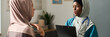 © pressmaster - Two Muslim women engaging in conversation in medical environment wearing hijabs and discussing healthcare details with clipboard. Woman with stethoscope showing attentive expression