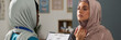 © pressmaster - Two Muslim women engaged in discussion in medical office, one wearing stethoscope and scrubs, another in hijab expressing concern, demonstrating interaction between patient and healthcare provider