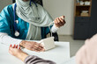 © pressmaster - Muslim medical professional wearing stethoscope, holding patient's hand, performing consultation in clinic setting