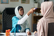 © pressmaster - Muslim healthcare worker wearing hijab assessing patient's temperature in clinical setting. Room contains medical supplies and clipboard with notes on desk