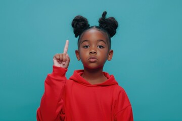 A young girl in a bright red hoodie holds up her hand in a peace sign gesture