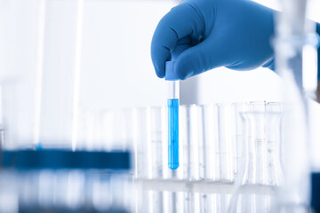 a scientist's hand in a medical glove holds a test tube with a substance