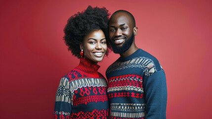 African American couple in festive Christmas sweaters, laughing together against a red background.