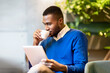 © Prostock-studio - Reading News. Happy afro man using digital tablet computer and drinking coffee sitting in modern cafe, copyspace
