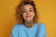 © JAYDESIGNZ - Young woman with curly hair and tatoos in casual blue sweatshirt smiling against orange background for advertising and promotion